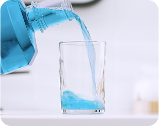 Pouring antibacterial mouth rinse into a glass as part of implant denture oral hygiene and maintenance routine.