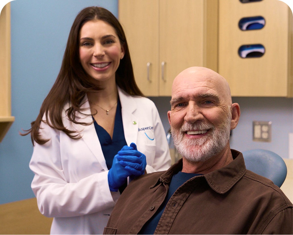 Male patient and Aspen Dental provider smiling together after a denture fitting, promoting the Denture Money-Back Guarantee.