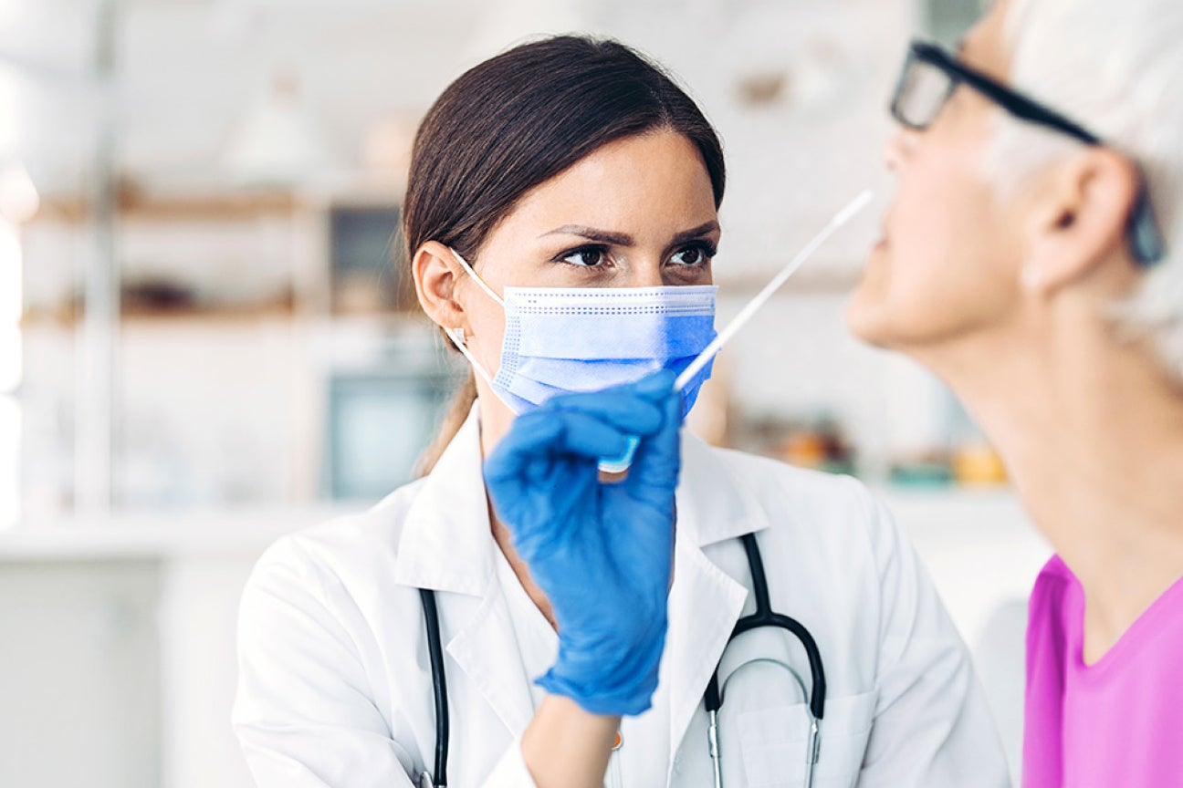 A medical provider assisting a patient with a nasal swab for a PCR test.