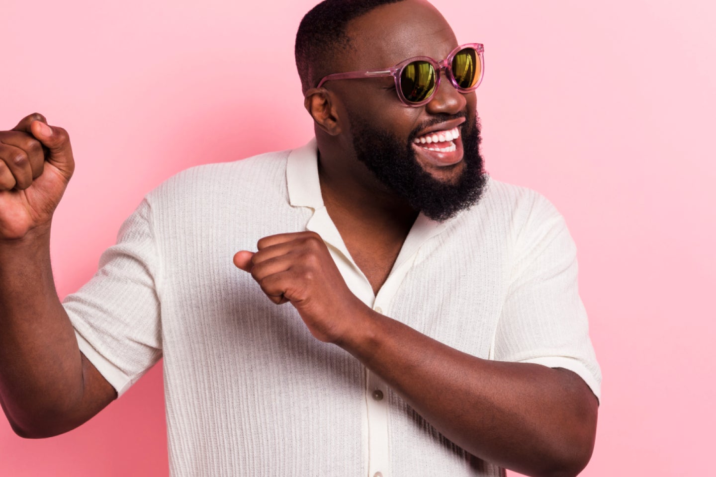 A joyful man wearing sunglasses dances against a pink background, showcasing his confidence and happiness, likely as a result of his clear aligner treatment with Motto. His bright smile reflects the positive outcome of orthodontic care.