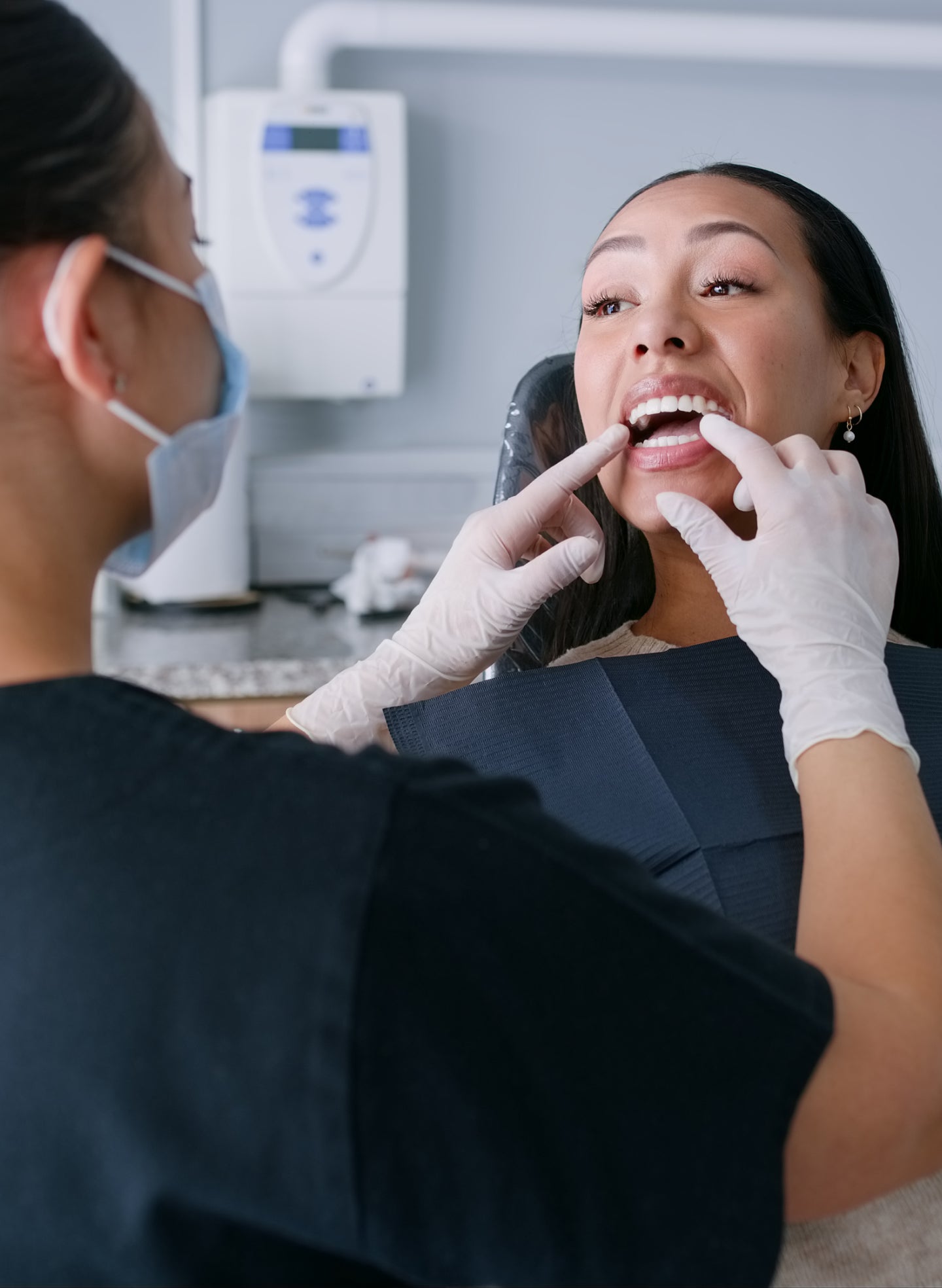 A dentist in gloves examines a smiling patient's teeth during a consultation, discussing potential side effects of dental implants at ClearChoice.