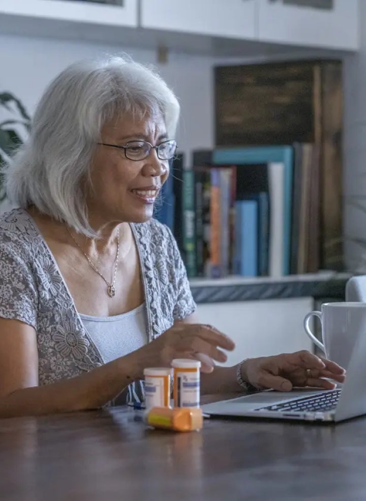 An elderly woman is sitting at a table using a laptop computer.
