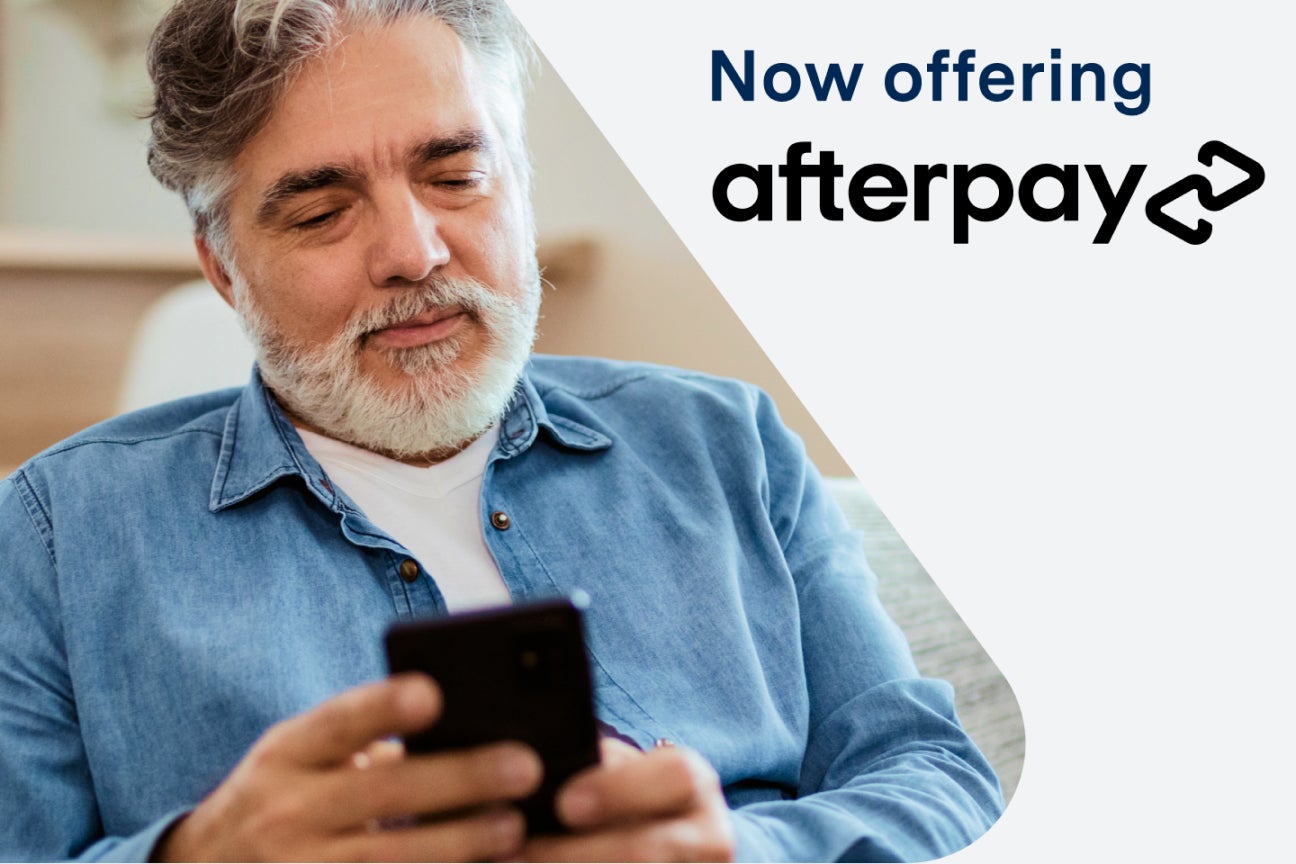 A man sitting on a couch looking at his phone with the words now offering afterpay behind him