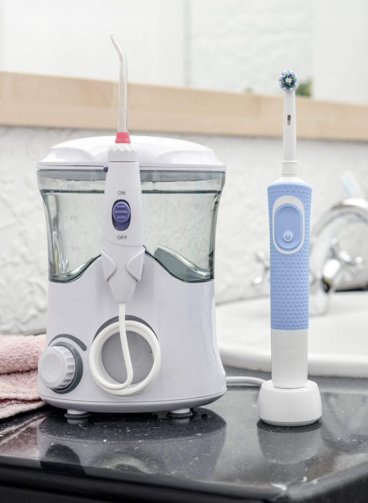 A ClearChoice dental hygiene setup featuring a water flosser and an electric toothbrush placed on a bathroom counter. The image shows essential tools for maintaining oral hygiene, particularly for dental implant care.