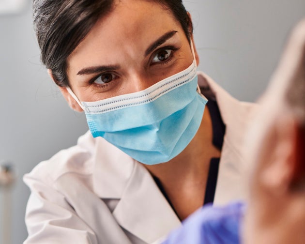 A dentist wearing a mask attentively examining a patient, emphasizing personalized consultations for tooth cap treatments at Aspen Dental.