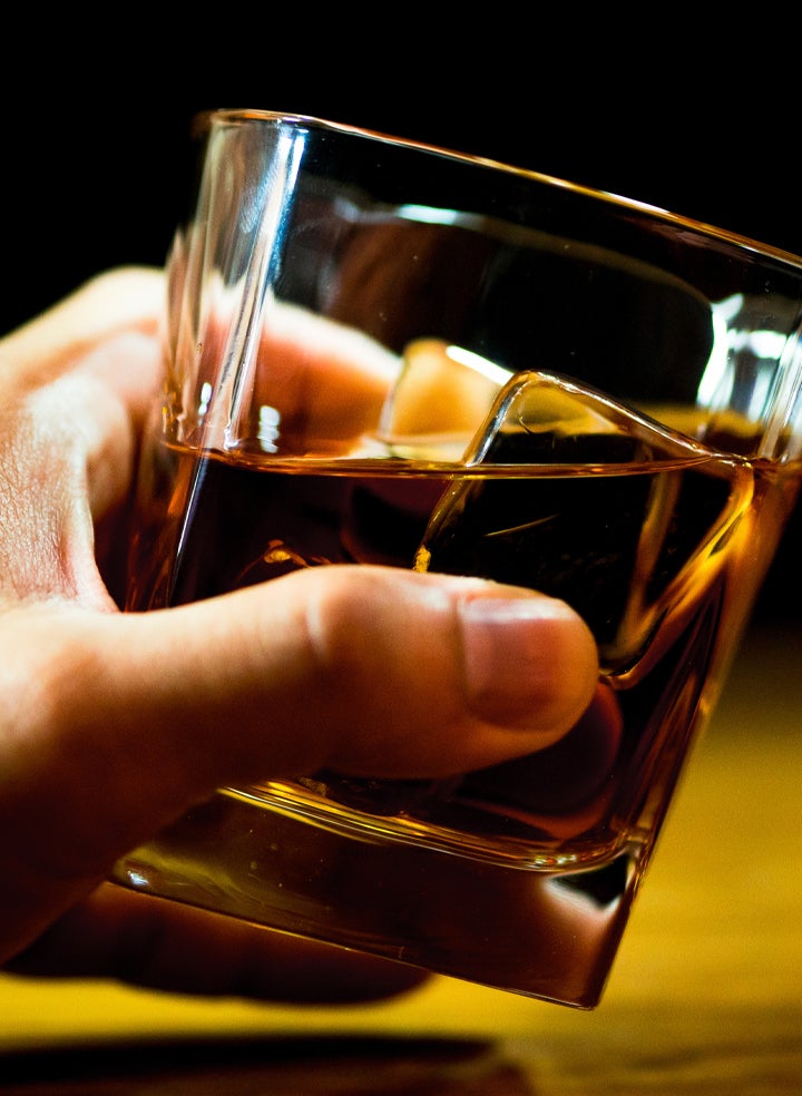 A person is holding a glass of whiskey with ice cubes