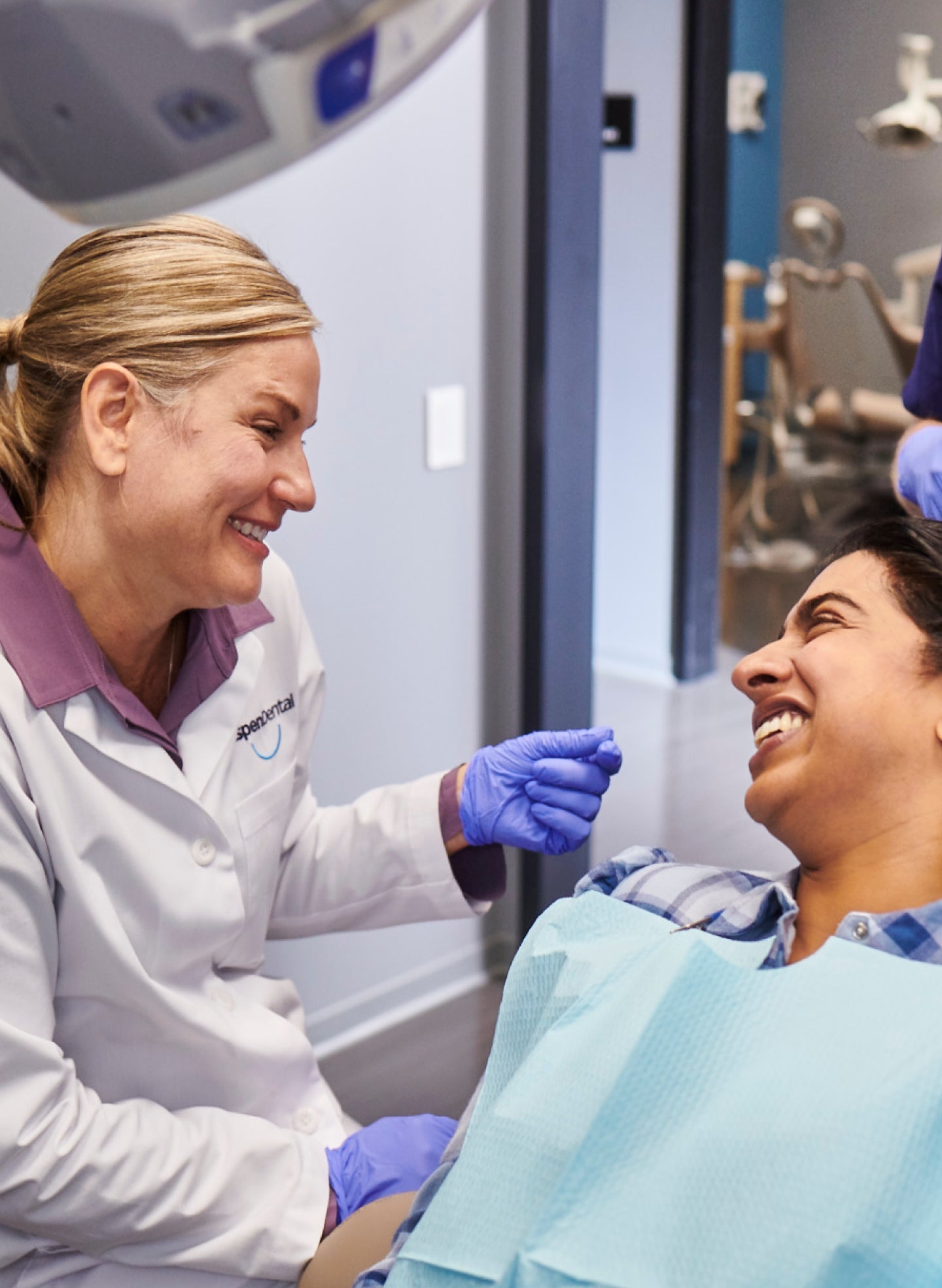 Aspen Dental hygienist smiling while providing a dental cleaning to a patient in a modern clinic setting.