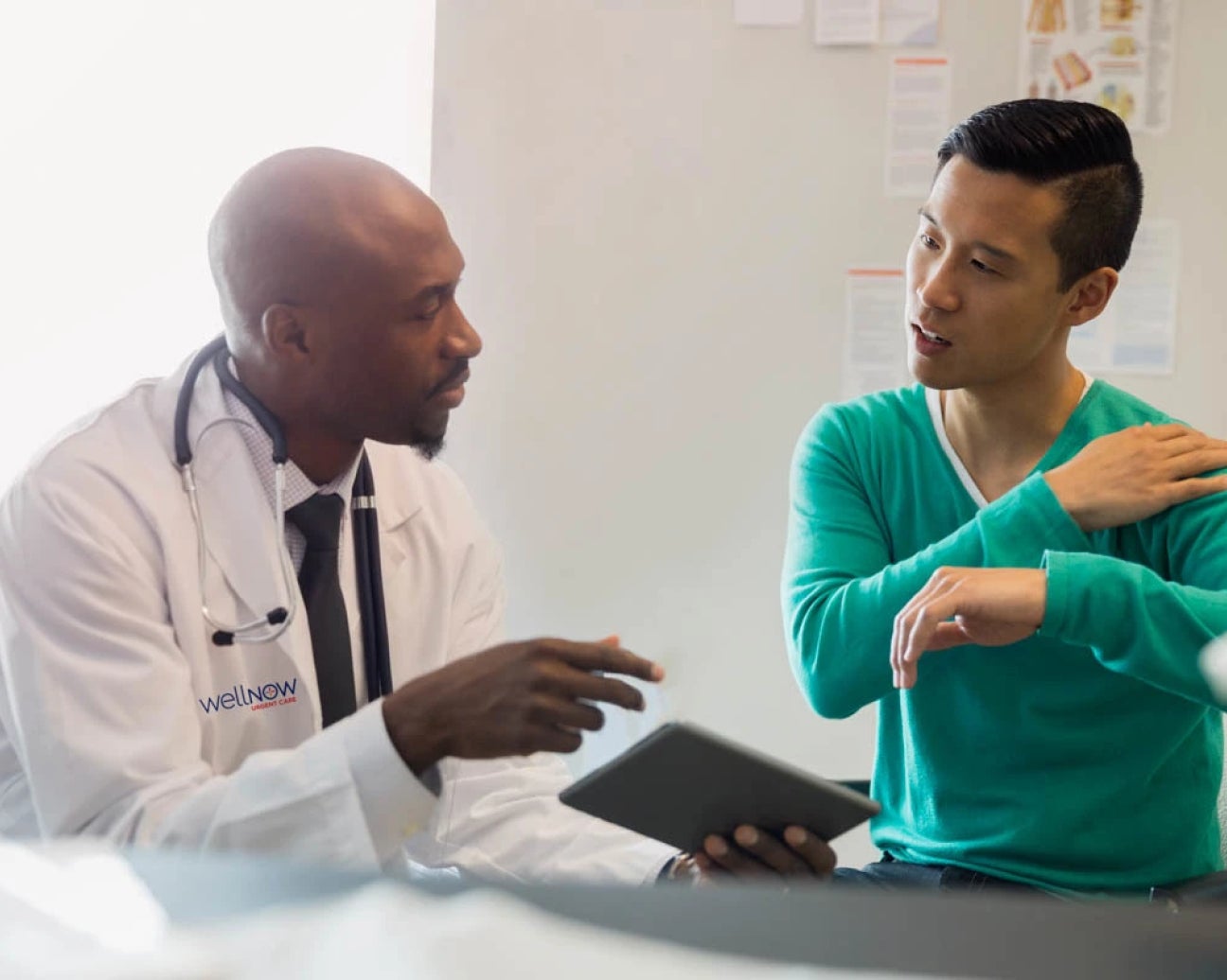 A patient is holding their shoulder and lifting their arm up, explaining a health issue to a medical provider.