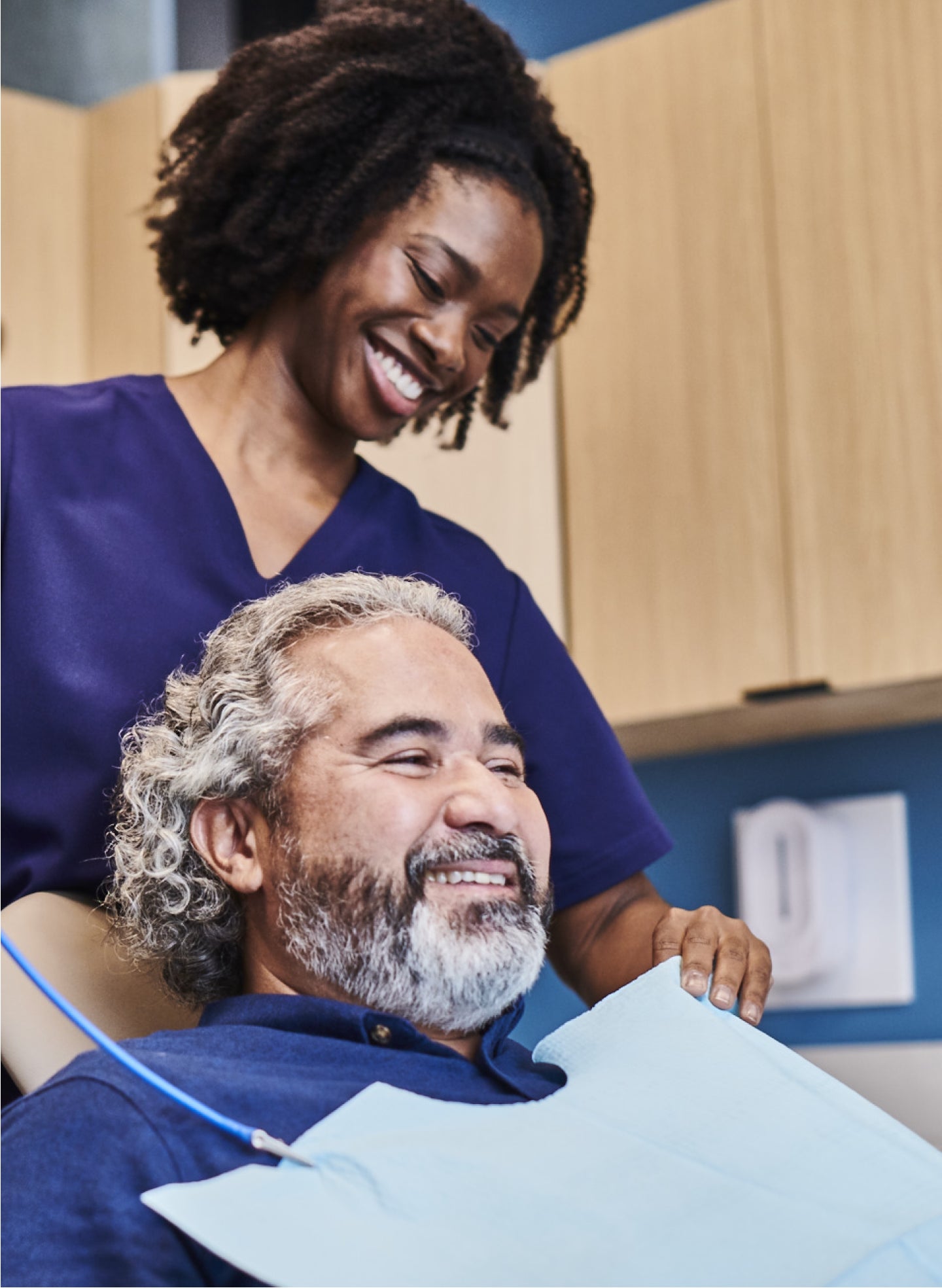 A woman in purple scrubs is smiling at a man in a dental chair