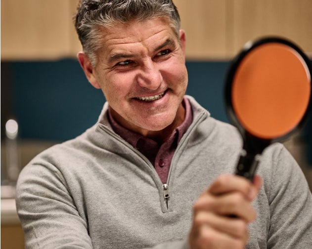  A happy patient holding a mirror and smiling after receiving tooth caps, showcasing satisfaction and high-quality dental care at Aspen Dental.