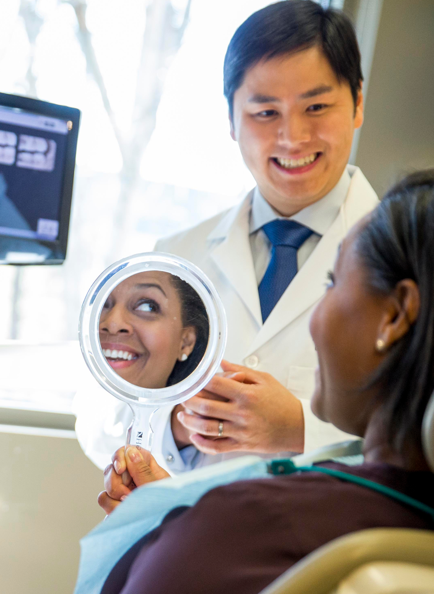 A dentist shows a patient their smile using a round mirror during a consultation. The scene highlights one type of dental image: patient interaction in a clinical setting.