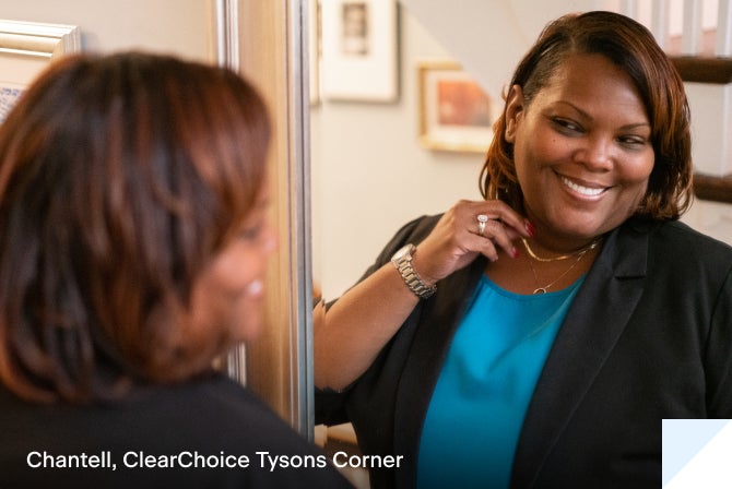 Chantell, a ClearChoice dental implant patient, standing in front of a mirror smiling.