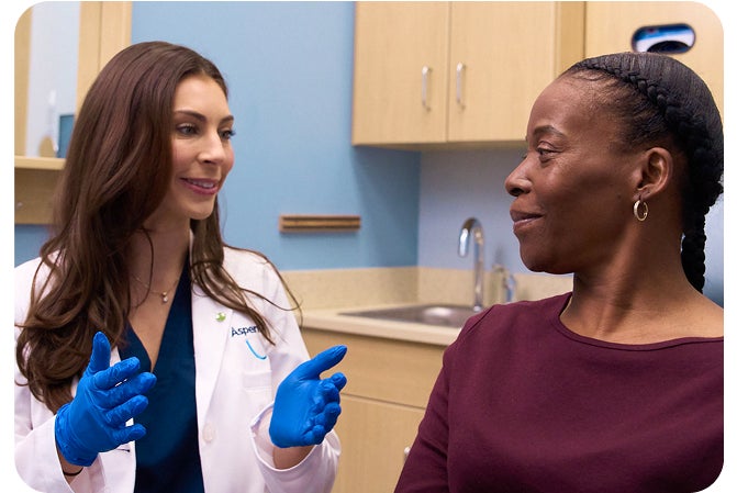 Aspen Dental dentist wearing blue gloves discussing denture care services, care team support, and same-day appointments with a smiling patient in a clinical setting.