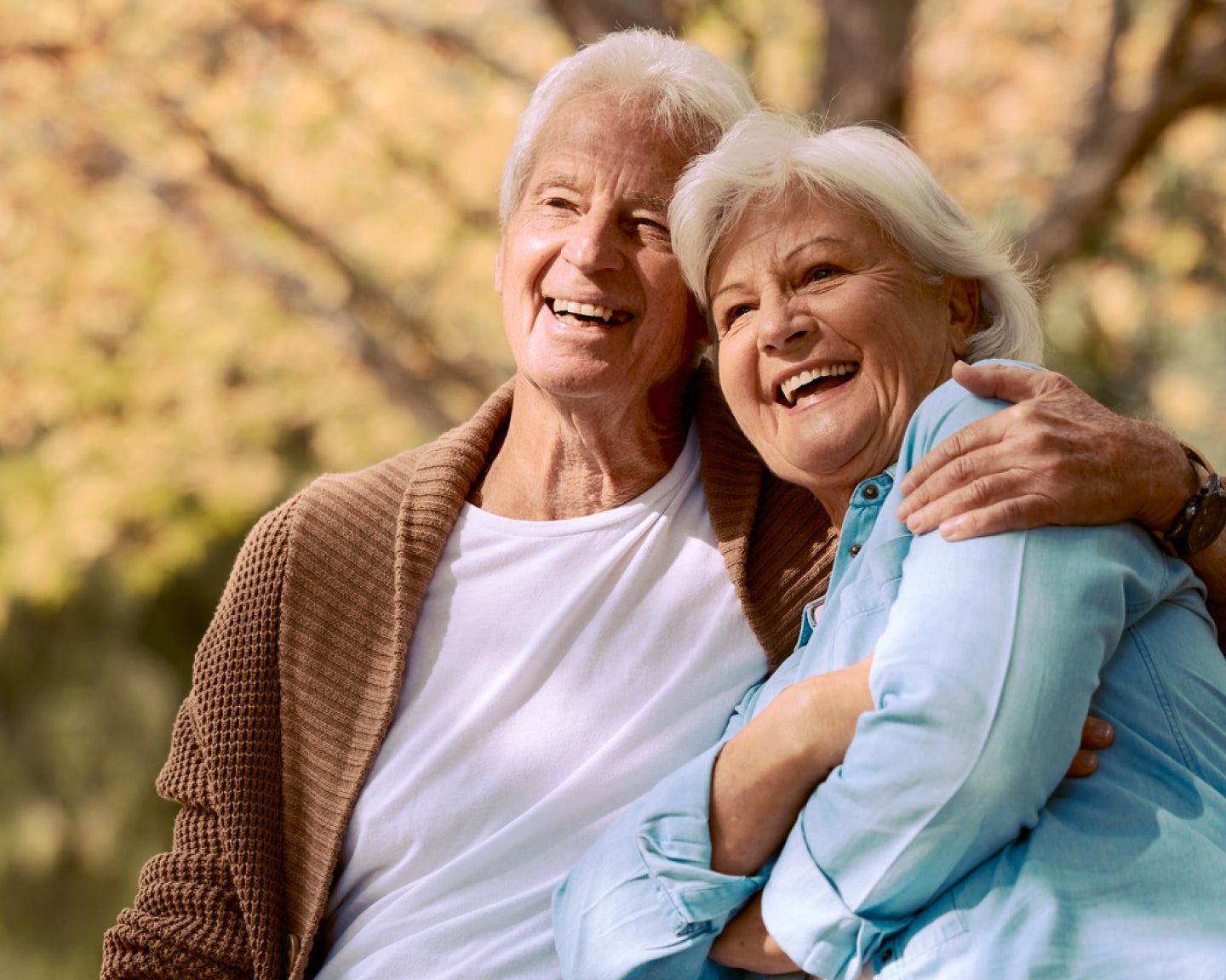 A joyful senior couple embracing outdoors, showcasing confidence and happiness with healthy smiles achieved through Aspen Dental care.