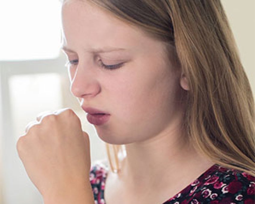 A young girl covering her mouth while coughing