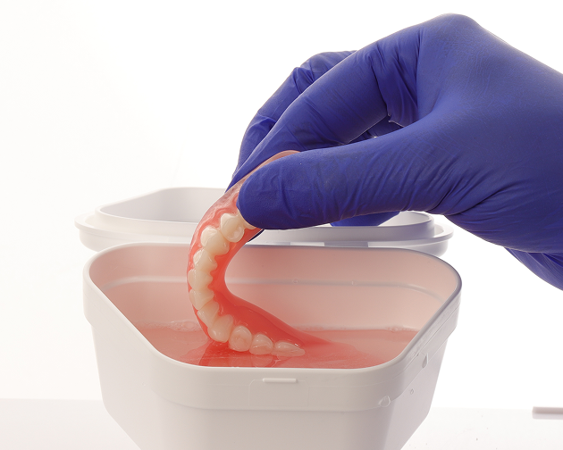 A person placing cleaned dentures into water or denture solution for proper storage. Aspen Dental highlights the importance of keeping dentures hydrated and ready to use.
