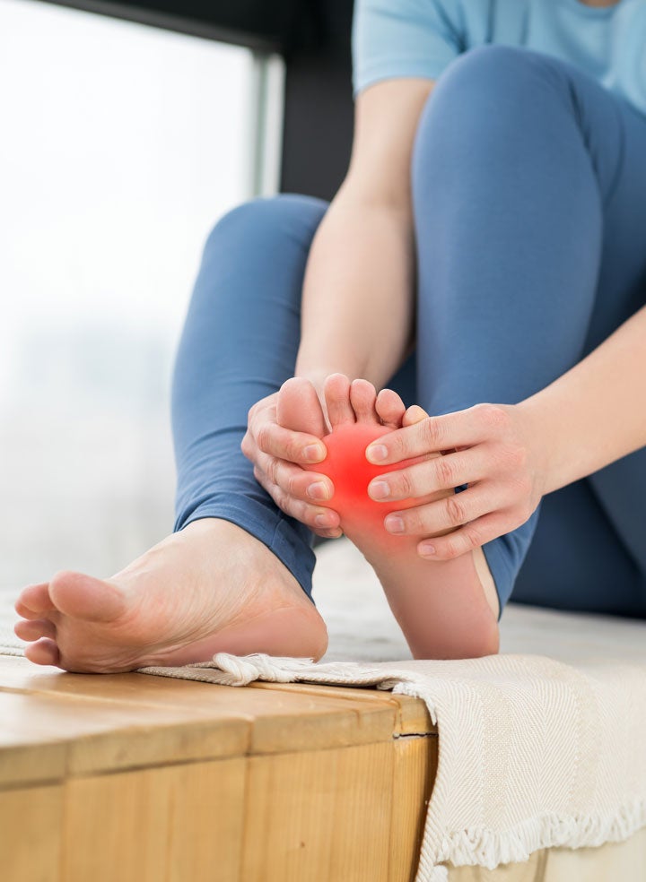 a close up photo of someone holding their foot, there is a red highlight on the bottom of their foot to signify pain.