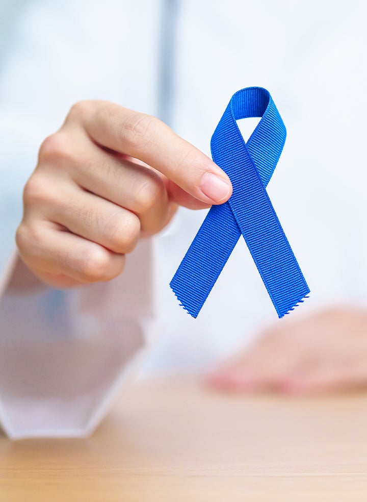 A person is holding a blue ribbon in their hand representing colorectal cancer awareness.