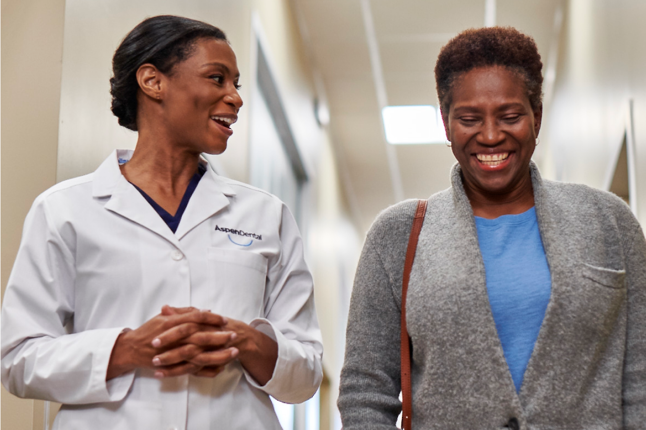 A smiling patient walking alongside a dentist in the hallway, representing compassionate care and expert guidance for tooth cap solutions at Aspen Dental.
