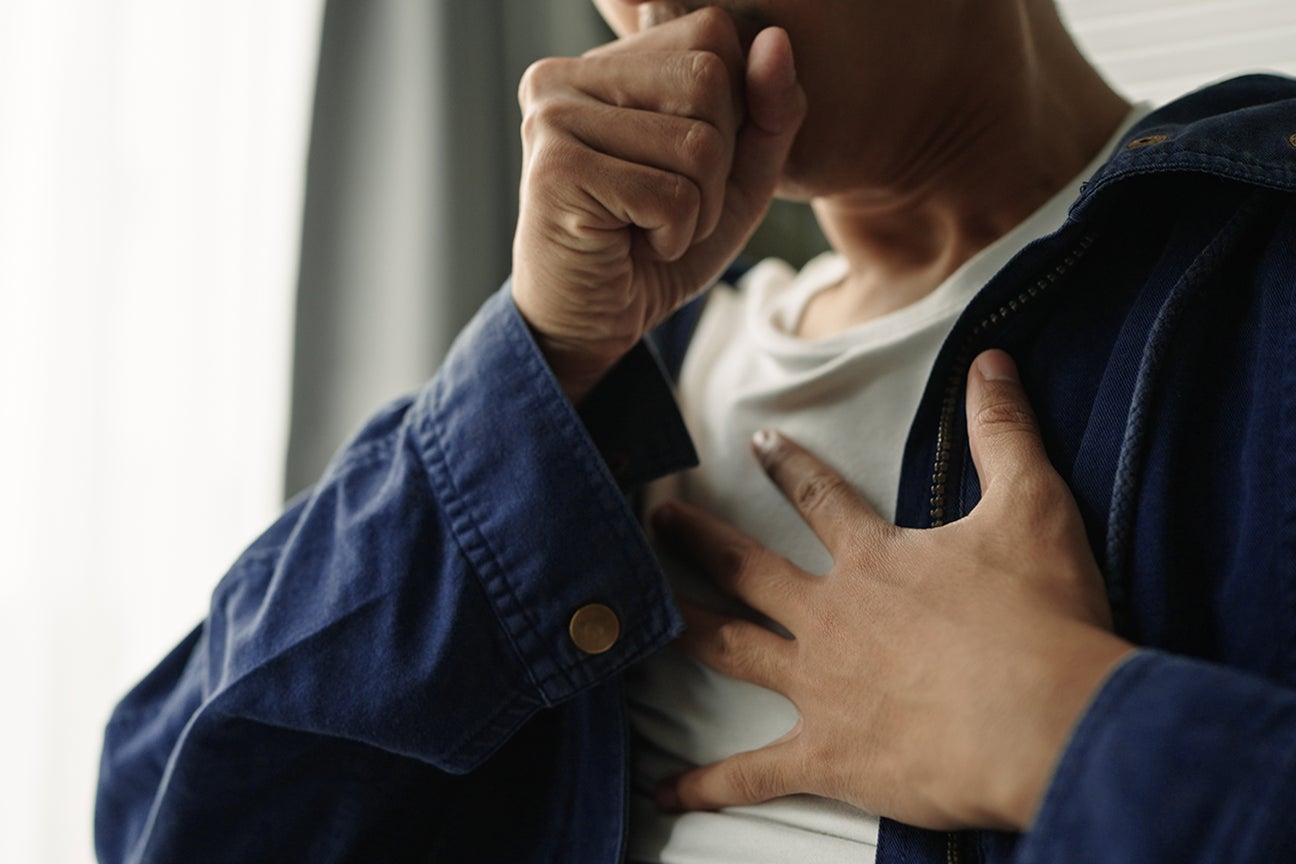 A close up photo of a person coughing and holding their chest.