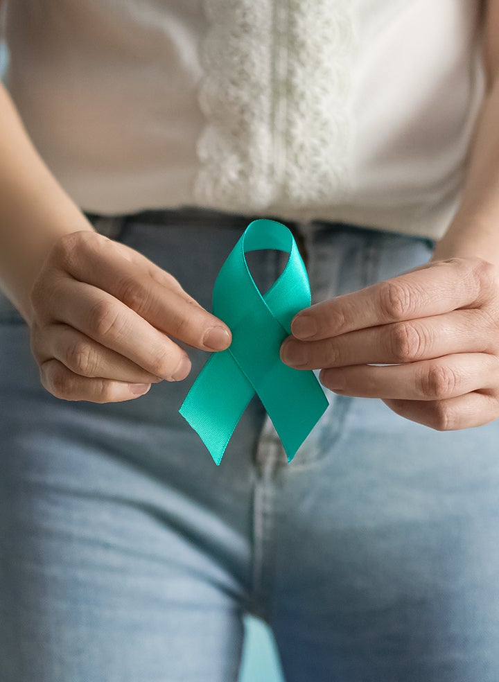 A woman holding a cervical health awareness ribbon at waist level.