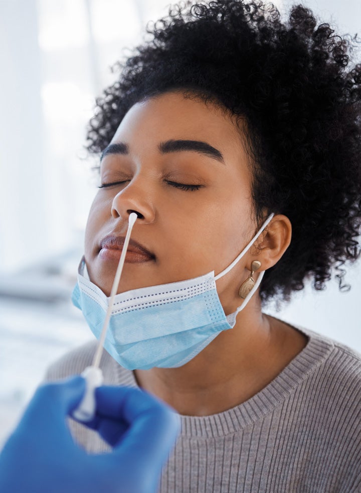 A medical patient with their mask pulled down; a doctor’s hand holds a swab in the patient’s nose to test for COVID-19. 