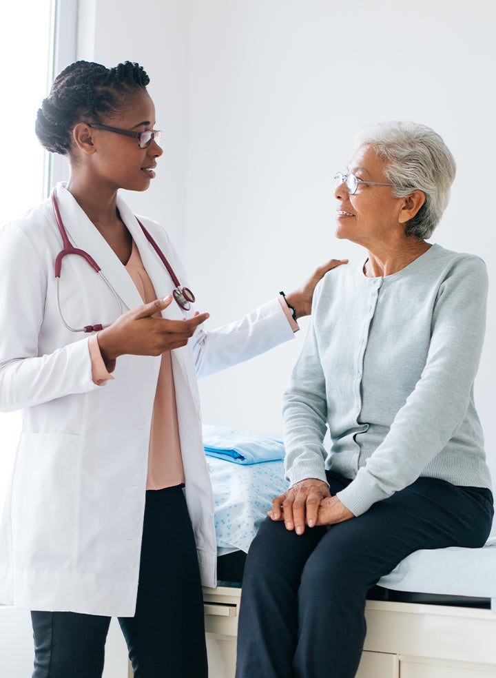 A doctor is talking to an older woman who is sitting on a bed