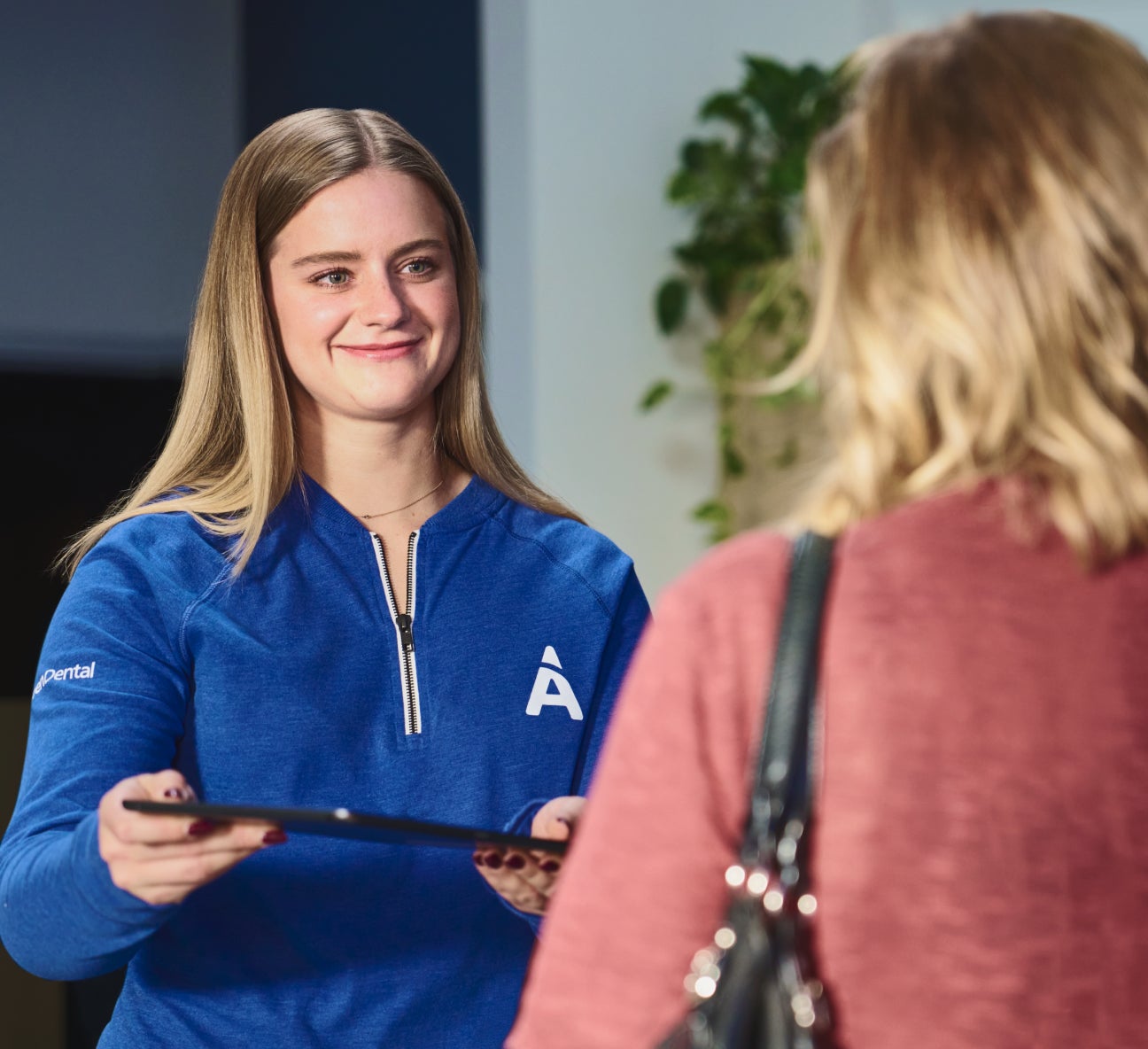 Aspen Dental team member at the front desk handing a clipboard to a patient, representing a welcoming and seamless dental cleaning experience.