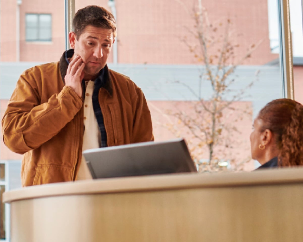 A man in a brown jacket speaks to an Aspen Dental receptionist. 