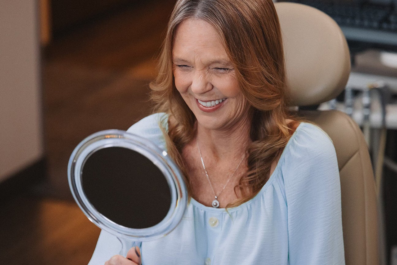 A woman is smiling while looking at herself in a mirror.