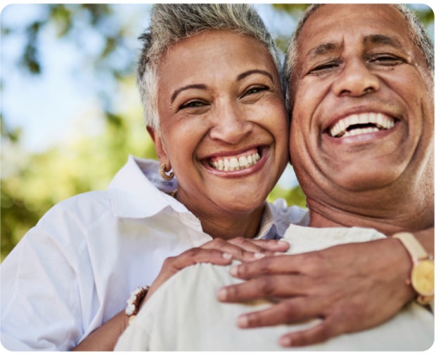 A joyful senior couple embracing and smiling outdoors on a sunny day, highlighting Aspen Dental's expertise in titanium dental implants and their commitment to bright, healthy smiles for all ages.