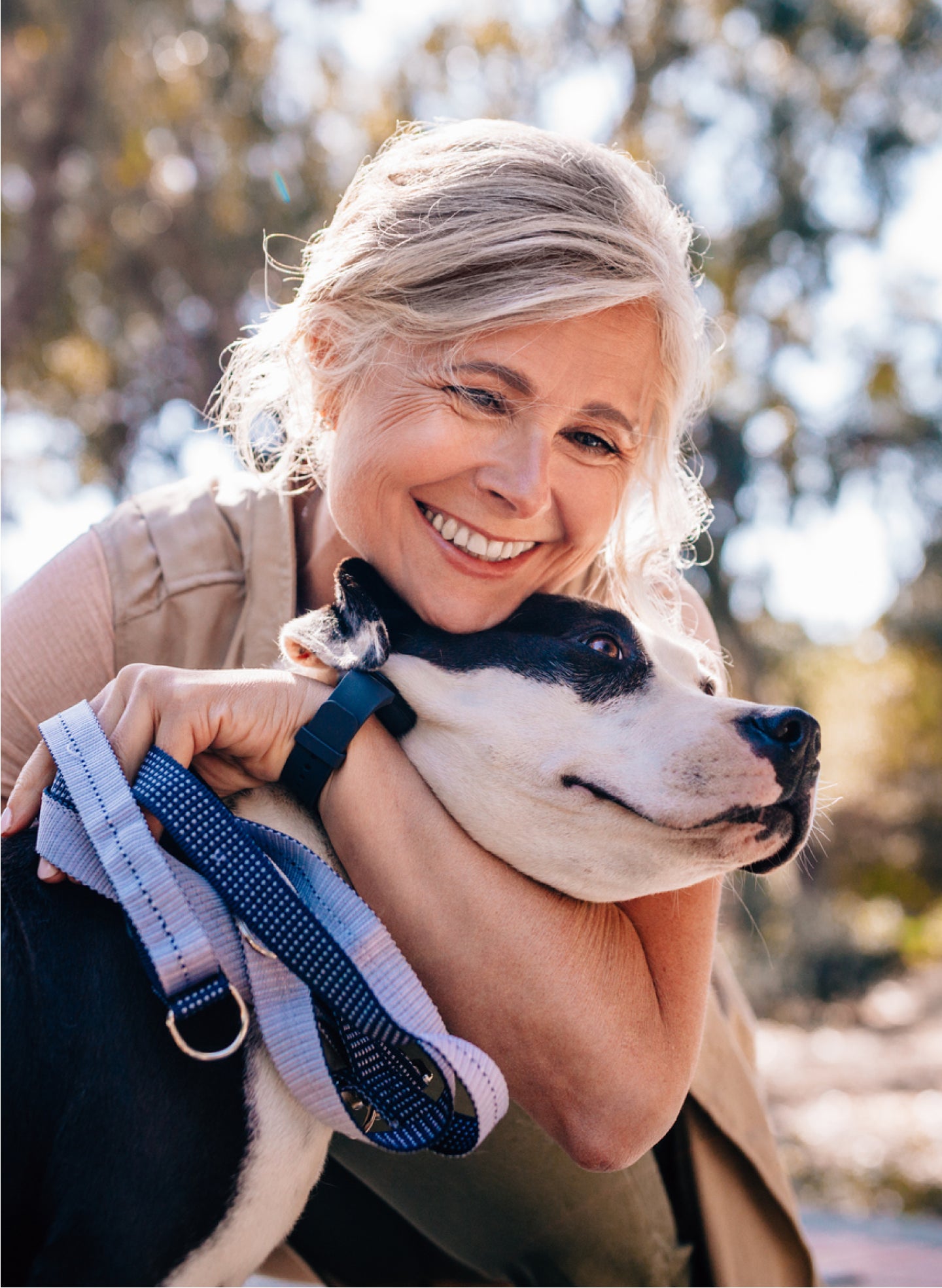 A woman is hugging a black and white dog on a leash