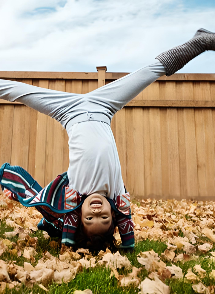 A child is doing a handstand in a pile of leaves.