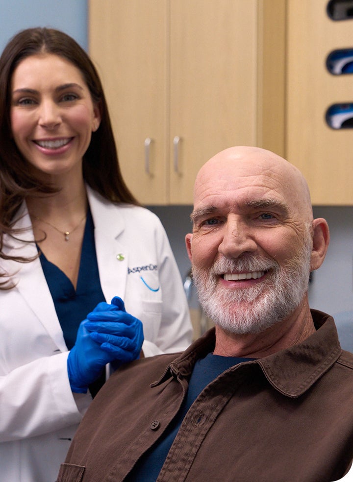 A smiling dentist stands beside an older male patient in a clinic, representing a successful dental visit. This image relates to oral health and managing conditions like canker sores.