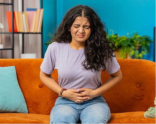 Woman sitting on a couch holding groin or abdomen region with a urinary tract infection.