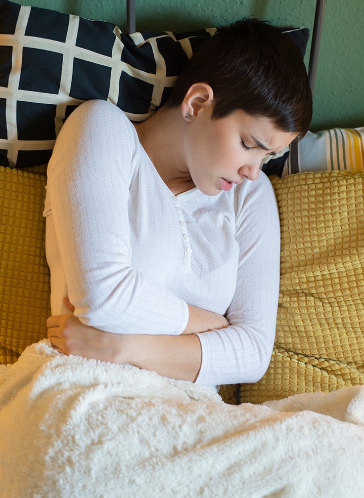 A woman is sitting on a couch with her hands on her stomach in pain