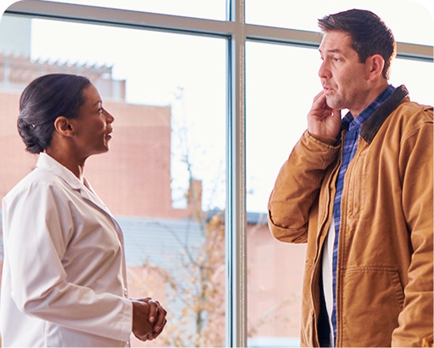 Male patient speaks with a female dentist near a window inside an Aspen Dental clinic, reflecting same-day emergency dental services.