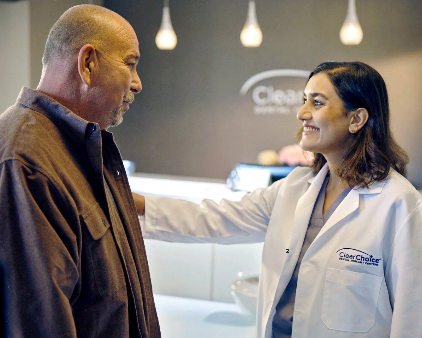 A ClearChoice doctor in a white lab coat speaking with a male patient on his options for financing his full mouth dental implant procedure. 