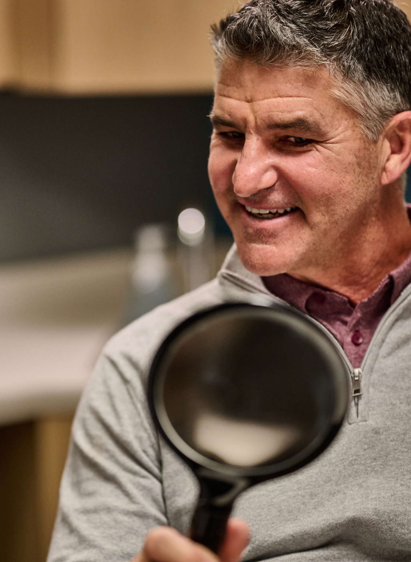 A mature man smiling while holding a magnifying glass, reflecting attentive and personalized dental care services at Aspen Dental.