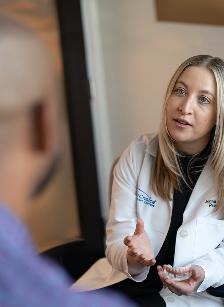 A woman in a lab coat is talking to a man in a blue shirt.