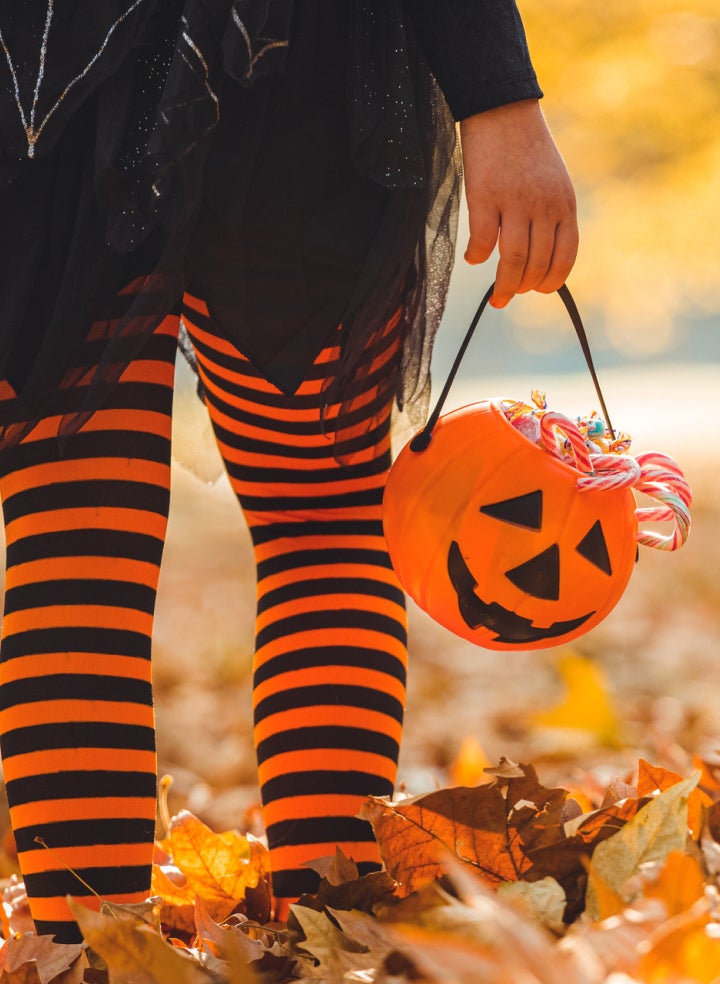 A little girl dressed as a witch is holding a pumpkin bucket on Halloween. 