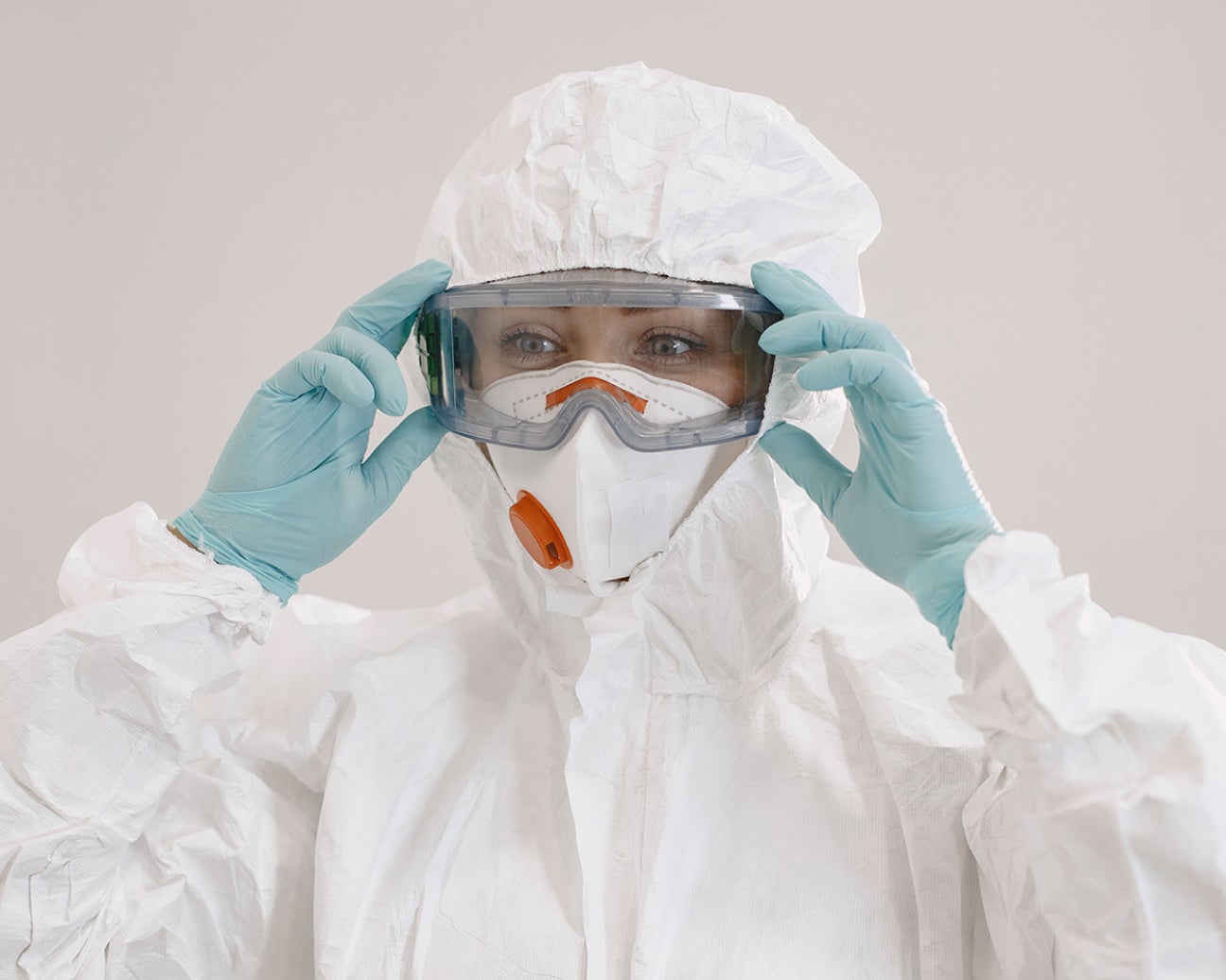 A person wearing a protective suit and respirator, putting on safety goggles.
