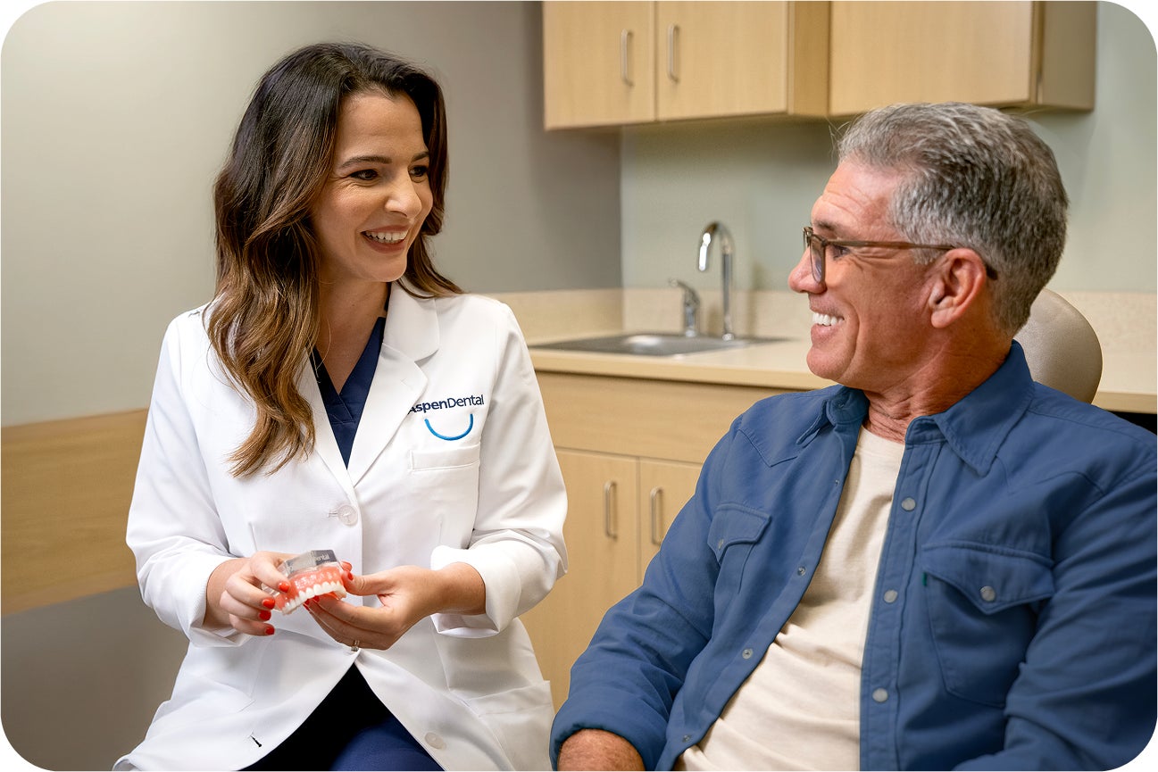 A smiling Aspen Dental provider discusses the single tooth implant treatment package with a male patient during an in-office consultation, highlighting what's included in the plan.