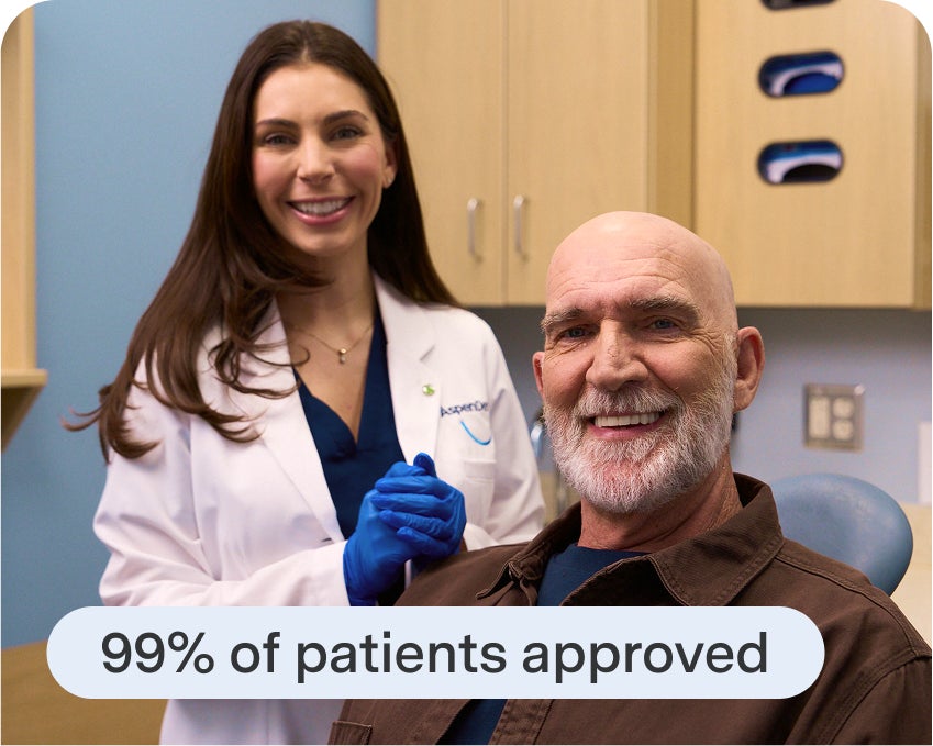 An Aspen Dental patient smiles while seated in a treatment chair, with a dental professional standing nearby—capturing the satisfaction and confidence that can come from accessible dental financing.