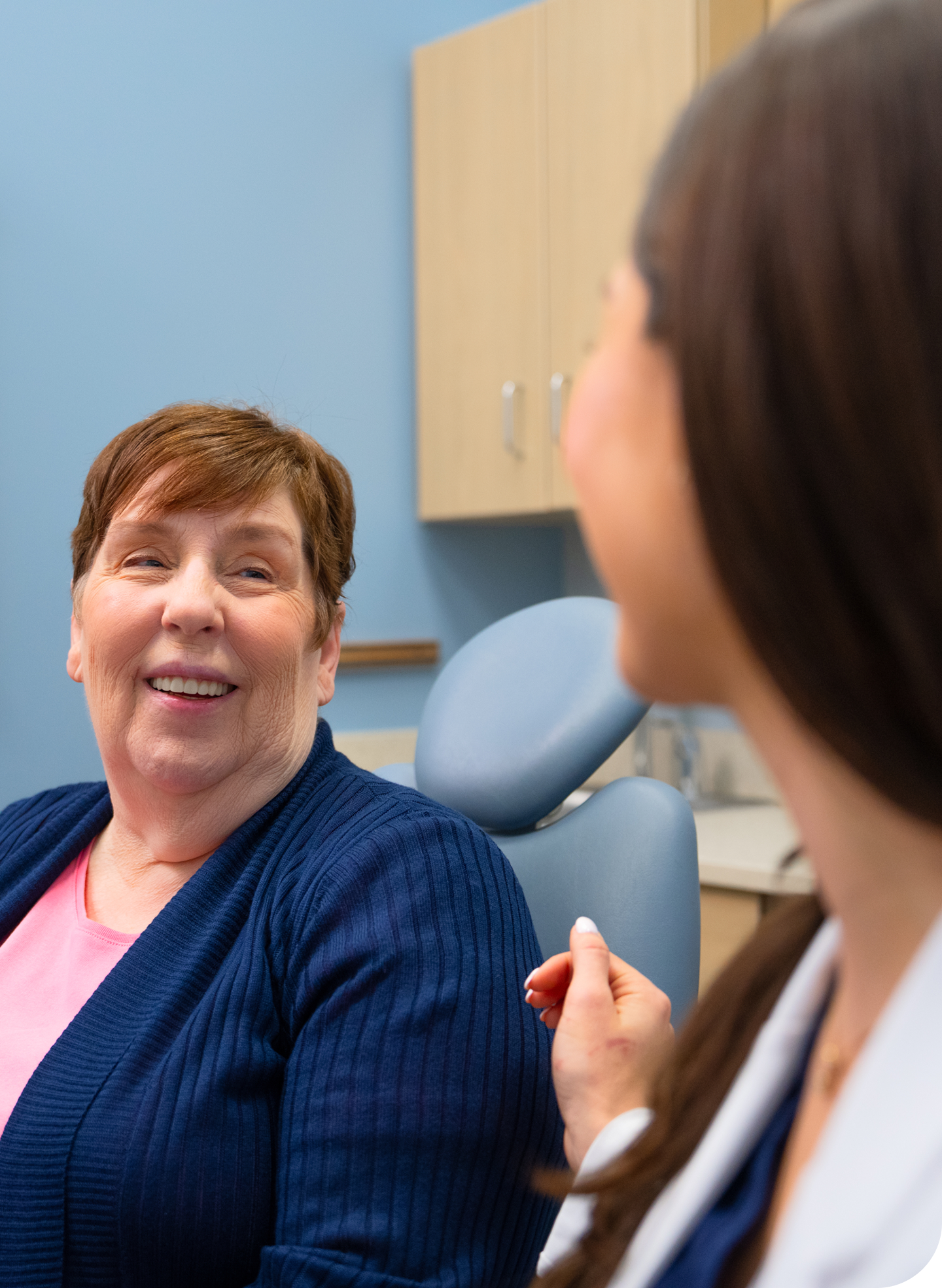A patient smiles while talking to a dental professional in a treatment room. They discuss cold sores and canker sores. The image shows a dental chair and cabinets in the background, highlighting oral health care.