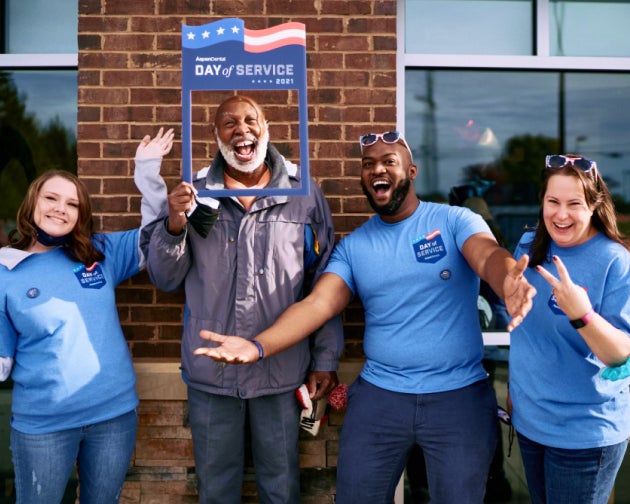 A group of Aspen Dental team members celebrating with a joyful patient in front of an Aspen Dental clinic, showcasing community impact and smiles.