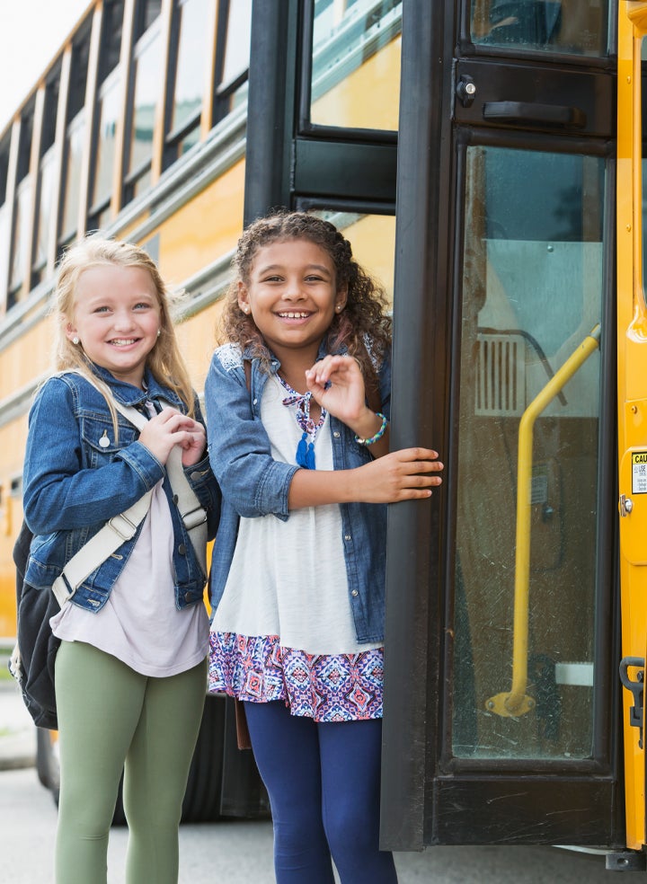 Two young girls are standing next to a school bus