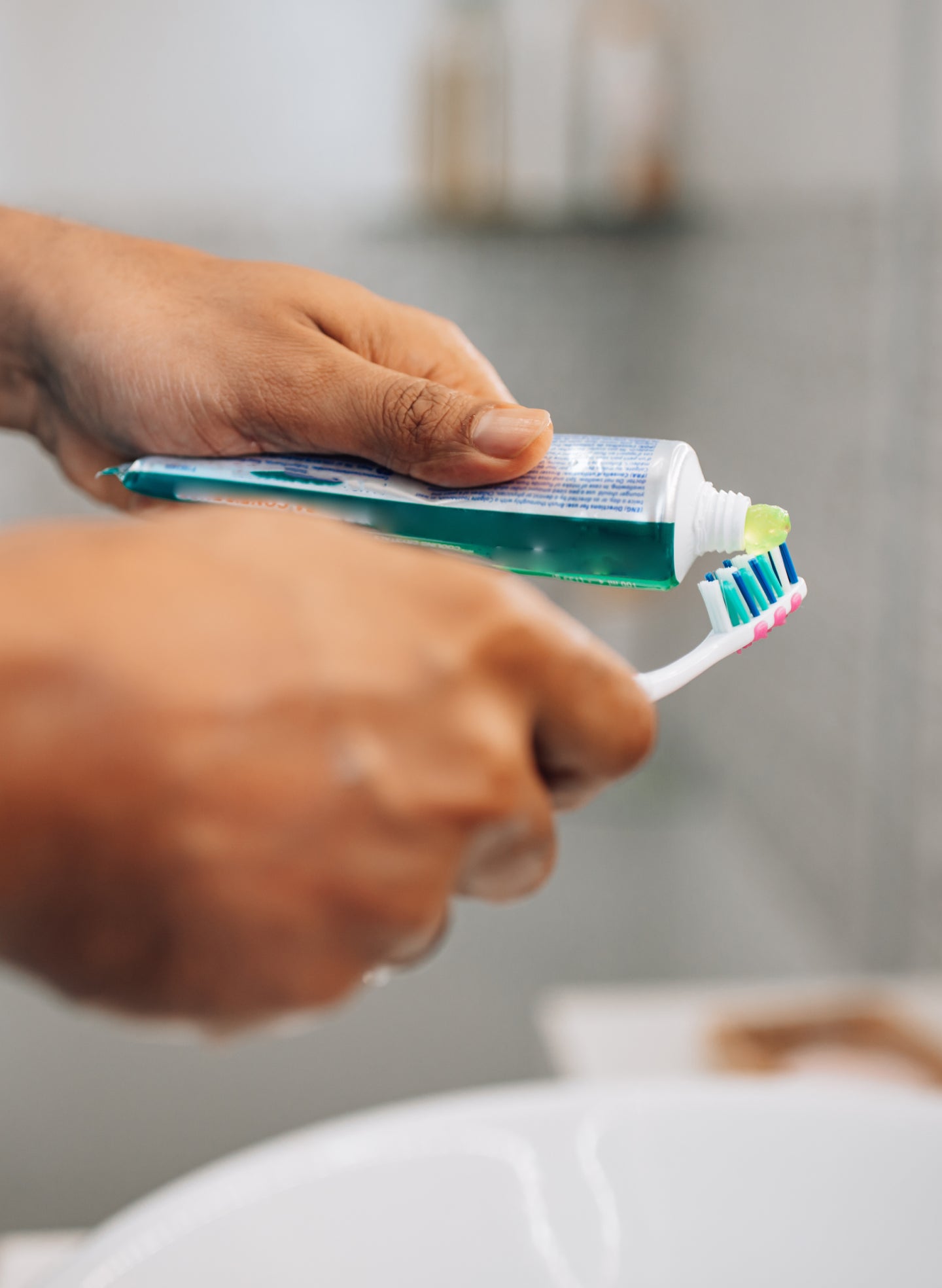 Close-up of a hand applying green toothpaste onto a toothbrush, focusing on dental hygiene, recommended by ClearChoice for gum disease care.