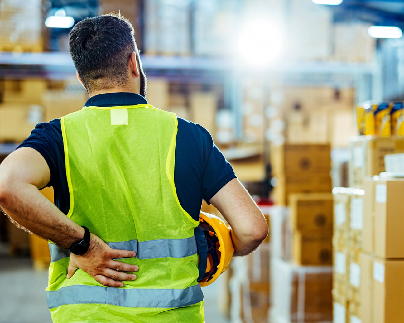 An employee wearing a safety vest, holding their back in pain.