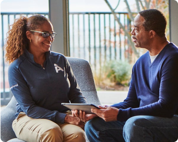  A smiling Aspen Dental team member in branded attire consulting with a patient in a comfortable setting, discussing titanium dental implants as a durable and effective solution for restoring smiles.